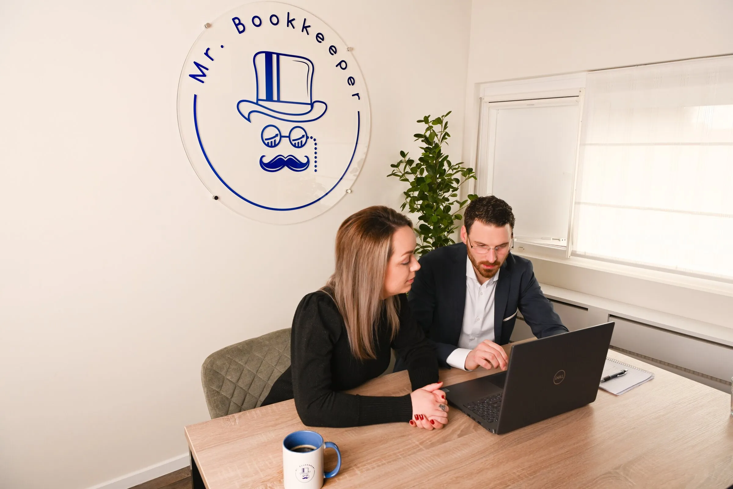 Twee mensen bekijken samen een administratie op de laptop, bij Mr. Bookkeeper met het logo aan de muur